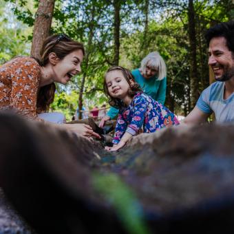 Mother, father and daughter laughing and playing in Babbling Brook, the water course part of our new adventure play area